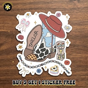 May include: A decorative sticker featuring a cowboy boot with a cow print pattern, a red hat, and a blue sky background. The boot displays the number 13 and the name TAYLOR. It includes blocks spelling TS, a beaded string with the text I KNEW IT Y I KNEW YOU, a bow, and various floral accents.
