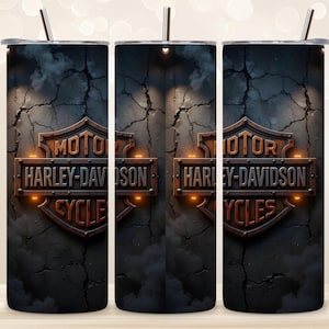 Op de afbeelding: Drie roestvrijstalen bekers met het Harley-Davidson-logo. Het logo heeft de vorm van een schild met de woorden "MOTOR HARLEY-DAVIDSON CYCLES" in een verweerd, metallic ontwerp. De achtergrond is een donker, getextureerd patroon met een rietje.