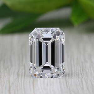 May include: A clear, emerald-cut diamond with a rectangular shape. The facets reflect light, creating a brilliant sparkle. The gemstone is set against a neutral background, highlighting its clarity and cut. The diamond's dimensions are approximately 10mm x 8mm.