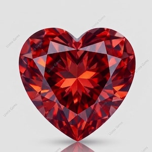 May include: A heart-shaped faceted gemstone in a deep, vibrant red color. The stone features a complex geometric cut with numerous triangular and kite-shaped facets that reflect light. The text Uzma Gems is repeated across the surface.