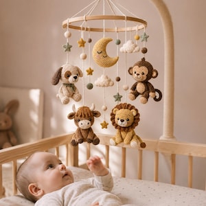 Può includere: Una giostrina per culla con figure all'uncinetto di un cane, una scimmia, una mucca highland e un leone, appese a una cornice circolare in legno. La giostrina include elementi all'uncinetto a forma di luna crescente sorridente, nuvole e stelle.
