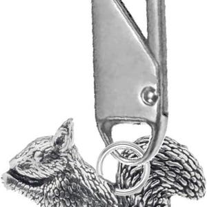 May include: A silver-colored keychain featuring a detailed squirrel charm. The squirrel is sculpted with textured fur and is attached to a metal clasp. The clasp is designed for easy attachment to keys or bags.