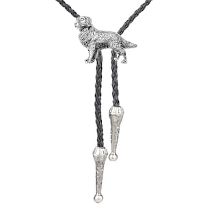 May include: Silver-coloured bolo tie with a detailed dog pendant. The dog is standing, with intricate fur detailing. The black braided cord has decorative silver tips, creating a classic Western accessory.