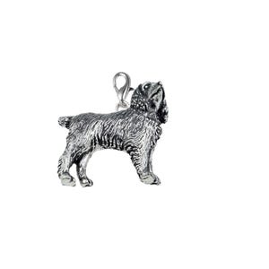 May include: A silver dog charm with a detailed textured coat and a clasp. The dog is standing and looking upwards. The charm is designed to be attached to a bracelet or necklace.
