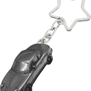 以下が含まれることがあります： 銀色の車の形をしたキーホルダー。星型のキーリングが付いています。車には、車輪や窓などの詳細な特徴があります。キーホルダーは金属製で、鍵を保持するように設計されています。