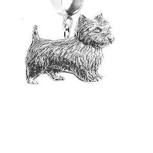 May include: A silver-coloured charm depicting a terrier dog. The charm has a detailed, textured surface and a ring at the top for attaching to a bracelet or necklace. The dog is standing, with its tail up and ears perked.