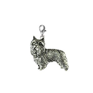 Puede incluir: Un charm de color plateado con forma de perro Cairn Terrier. El charm tiene una apariencia texturizada, con una representación detallada del pelaje y las características del perro. Incluye un pequeño cierre.