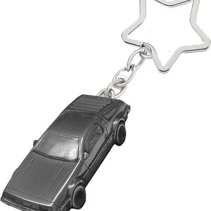 Könnte beinhalten: Ein silberfarbener Autoschlüsselanhänger mit einem sternförmigen Schlüsselring. Das Auto ist ein detailliertes Miniaturmodell. Der Schlüsselanhänger ist aus Metall und wahrscheinlich ein Sammlerstück. Die Abmessungen des Autos sind ca. 7 cm lang.