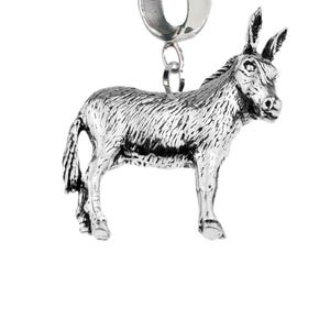 May include: A silver-toned metal charm shaped like a donkey, featuring detailed fur texture and a standing pose. The charm is attached to a smooth, circular silver-toned bail at the top, designed for threading onto a bracelet or necklace chain.