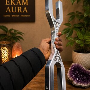 May include: A large, silver-coloured metal tuning fork with a dual-pronged design at both ends. The device features triangular cutouts and is clearly engraved with the text 128Hz on one of the lower prongs, indicating its specific frequency.
