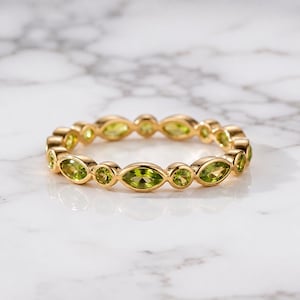 May include: A gold band ring featuring an alternating pattern of marquise-cut and round-cut light green peridot gemstones set in a continuous eternity style. The metal has a polished finish, and the stones are arranged in a repeating sequence.
