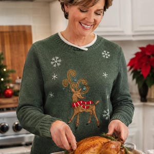 May include: A dark green long-sleeve sweater featuring an embroidered reindeer wearing a red and white scarf, accented with blue ornaments on its antlers and white snowflake patterns across the front, with a ribbed crew neckline and cuffs.