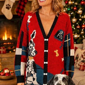 May include: A red V-neck knit cardigan featuring a black trim and white bone-shaped buttons. The sweater displays a graphic of a spotted dog, blue and black plaid sleeve patterns, and scattered bone motifs. The design includes a dark blue hem.