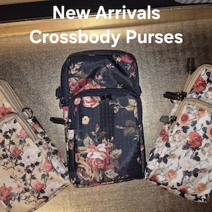 May include: Three rectangular crossbody purses featuring floral patterns. The left purse is beige, the centre is navy blue, and the right is white. Each purse has multiple zippered compartments and metal hardware. Text at the top reads: New Arrivals Crossbody Purses.