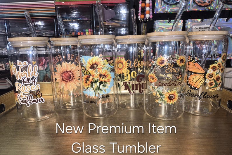 May include: Six clear glass tumblers with bamboo lids and glass straws, each featuring unique sunflower and butterfly designs with inspirational text like In a world full of roses be a sunflower, Always be kind, and You are my sunshine.
