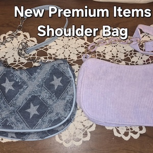 May include: Two shoulder bags with the text New Premium Items Shoulder Bag. One bag is dark blue denim with a frayed diamond and star pattern and a silver chain strap. The other bag is light purple corduroy with a matching purple chain strap.