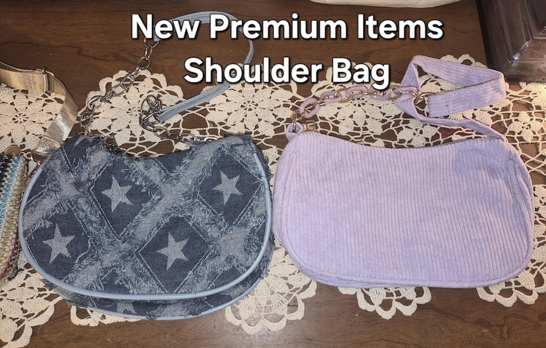 May include: Two shoulder bags with the text New Premium Items Shoulder Bag. One bag is dark blue denim with a frayed diamond and star pattern and a silver chain strap. The other bag is light purple corduroy with a matching purple chain strap.