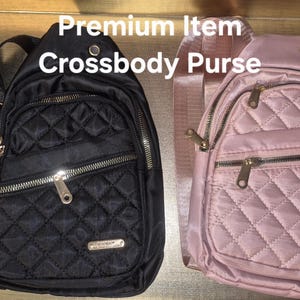 May include: Two crossbody bags, one black and one light pink, featuring a quilted diamond pattern, gold-tone metal zips, and adjustable straps. The text 'Premium Item Crossbody Purse' is displayed above the bags, which have a front pocket.