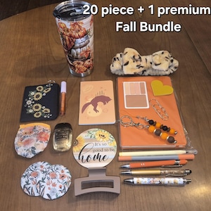 May include: A 20 piece + 1 premium Fall Bundle including a pumpkin-themed tumbler, a leopard print headband, a sunflower wallet, a fox notebook, an orange planner, pens, a floral pouch, hand sanitiser, a round sign, and hair accessories.