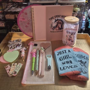 May include: A collection of horse-themed stationery and accessories including a spiral notebook, a glass tumbler with a bamboo lid, a pencil case, pens, bookmarks, stickers, a keychain, nail clippers, and light blue socks with the text Just a girl who loves horses.