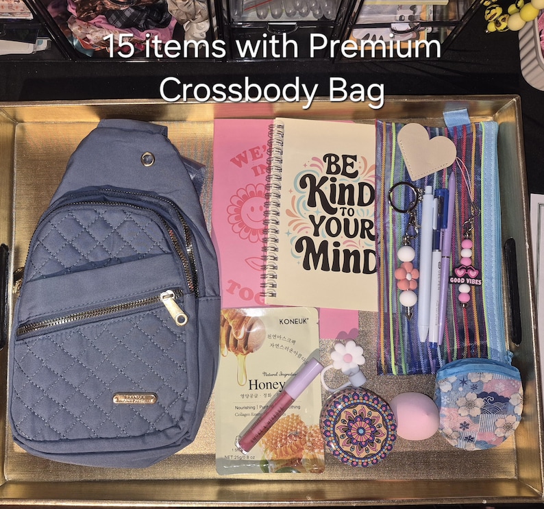 May include: A blue quilted crossbody bag with gold zips, a spiral notebook with the text BE KIND TO YOUR MIND, a striped pencil case, a honey face mask, a pink lip gloss, a floral compact mirror, a makeup sponge, and various keychains.