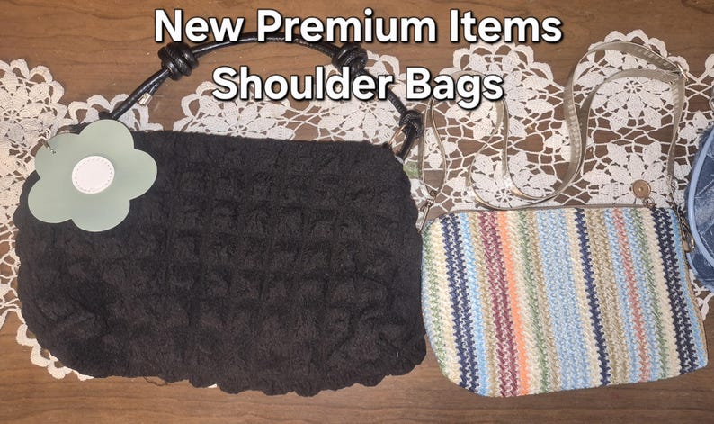 May include: Two shoulder bags with the text New Premium Items Shoulder Bags. One is a black textured bag with a light green flower-shaped tag and a black handle. The other is a rectangular bag with a multi-coloured striped pattern and thin straps.