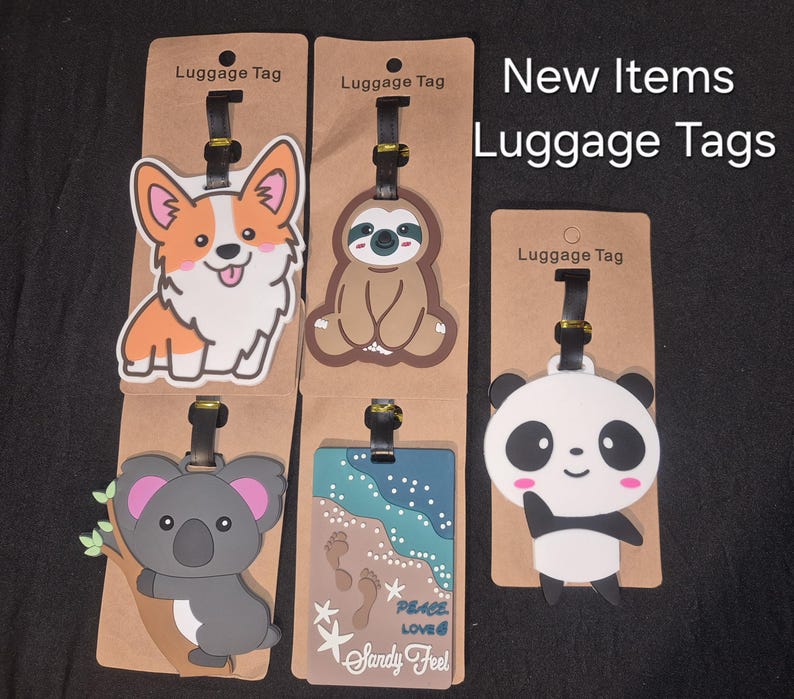 May include: Five luggage tags on brown cardboard backing labelled Luggage Tag. Designs include a corgi, a sloth, a koala on a branch, a beach scene with footprints and the text Peace Love Sandy Feel, and a panda. The text New Items Luggage Tags is visible.