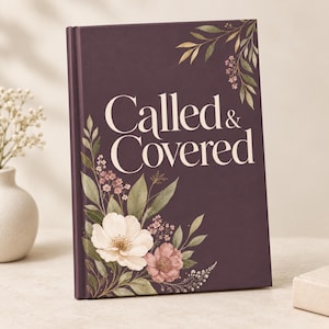 Op de afbeelding: Een hardcover boek met een donkerpaarse kaft met de witte tekst Called & Covered. Het ontwerp bevat illustraties in aquarel-stijl van groene bladeren, kleine roze bloemetjes en grote witte en roze bloemen in de hoeken van de kaft.
