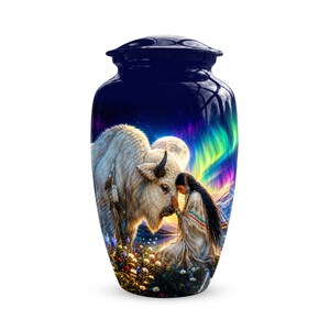 May include: A dark blue cylindrical cremation urn featuring a detailed graphic print of a white buffalo and a person kneeling in a field of flowers. The scene includes a full moon, a vibrant aurora borealis, and distant mountains under a night sky.