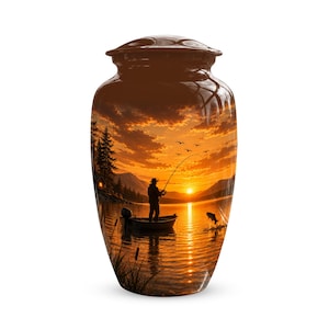 May include: A cylindrical cremation urn with a glossy finish featuring a printed scene of a person fishing from a small boat on a lake at sunset. The image displays a golden sky, silhouetted mountains, pine trees, and a fish jumping from water.