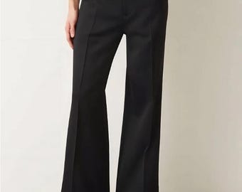 Puede incluir: Pantalones negros de talle alto con silueta de pierna ancha, cintura estructurada con trabillas, cierre de cremallera frontal y una raya marcada en el centro de cada pernera. Los pantalones se combinan con unos mocasines negros.