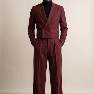 May include: A burgundy double-breasted suit with wide-leg trousers. The suit features a cropped jacket and is paired with a black roll neck. The outfit is a stylish ensemble for formal occasions.