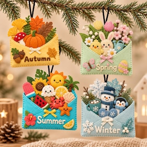 May include: Four felt envelope ornaments representing the seasons. The Autumn envelope features a pumpkin and leaves. The Spring envelope shows a rabbit, chick, and flowers. The Summer envelope displays a sun, crab, and ice cream. The Winter envelope depicts a snowman and snowflakes.