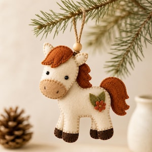 Può includere: Un ornamento in feltro a forma di cavallo con corpo color crema, criniera e coda color ruggine e zoccoli marrone scuro. Il cavallo ha occhi a perla neri e un piccolo dettaglio floreale sul fianco. È appeso a uno spago di juta con una perlina.