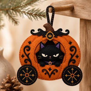 Può includere: Un ornamento in feltro a forma di carrozza a zucca con un gatto nero all'interno. La carrozza è arancione con volute nere, due ruote nere con accenti a stella dorati e un picciolo marrone. Un piccolo emblema a corona dorata si trova sopra il gatto.