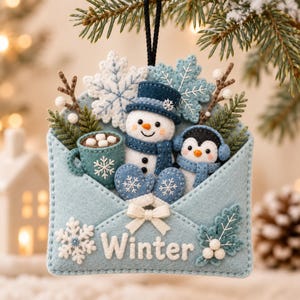 May include: A felt envelope ornament featuring a snowman in a blue hat and scarf, a penguin with earmuffs, a mug of hot cocoa with marshmallows, and snowflakes. The light blue envelope is decorated with a white bow and the word Winter in white.