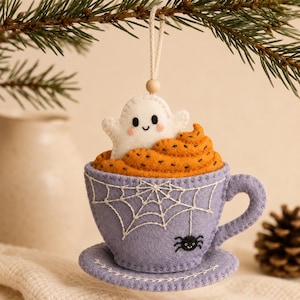 Peut inclure: Une décoration suspendue en feutrine en forme de tasse et soucoupe lavande. La tasse présente des toiles d'araignée brodées en blanc et une petite araignée noire. La tasse contient une garniture orange avec un petit fantôme blanc aux joues roses.