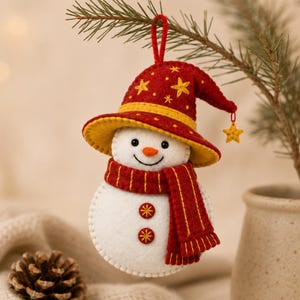 May include: A felt snowman ornament featuring a white body with two embroidered red and yellow buttons, a red scarf with yellow stitching, and a red pointed hat adorned with yellow stars and a dangling star charm hanging from a red loop.