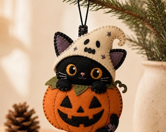 May include: A felt hanging ornament featuring a black cat wearing a cream-colored ghost-patterned hat, peeking out from inside an orange jack-o'-lantern pumpkin. The ornament has visible black stitching, green felt leaves, and a black hanging loop.