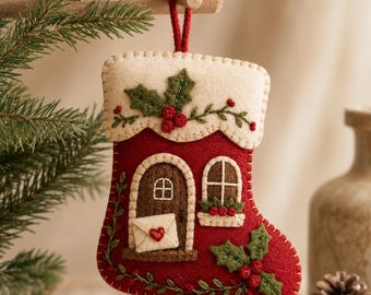 May include: A red felt Christmas stocking ornament featuring a cream-colored cuff with embroidered green holly leaves and red berries. The stocking displays a brown door with a white envelope and red heart, a window with a flower box, and green holly.