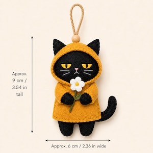 May include: A black felt cat ornament wearing a mustard yellow hooded raincoat and holding a white flower. It features a jute hanging loop with a wooden bead. The ornament measures approximately 3.54 inches tall and 2.36 inches wide as indicated.