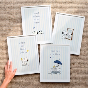 Pode incluir: Quatro quadros com moldura branca exibindo Snoopy e Woodstock sobre um fundo de listras azul-claras. As impressões apresentam as frases good things take time, you can do it, enjoy the little things e one day at a time com ilustrações.