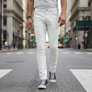 Op de afbeelding: Een slim-fit witte spijkerbroek met een klassiek ontwerp met vijf zakken, een knoopsluiting en zilverkleurige metalen klinknagels. De broek wordt gedragen met een effen lichtgrijs T-shirt en zwart-witte lage canvas sneakers.