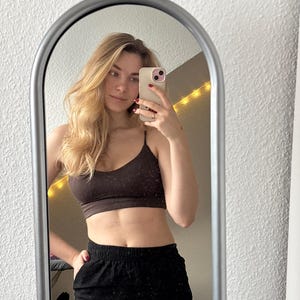 May include: A dark brown cropped camisole top with thin spaghetti straps and a scoop neckline, paired with black high-waisted pants featuring an elastic waistband. The garment is captured in a reflection within an arched silver-framed mirror.