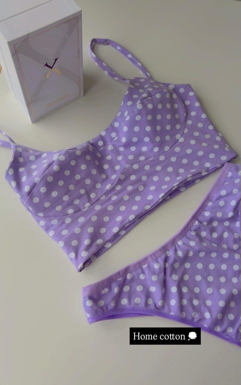 May include: A lavender two-piece set featuring a cropped top with thin straps and matching bottoms, both patterned with white polka dots. The set is labeled with the text Home cotton. A white rectangular box is positioned in the upper left corner.