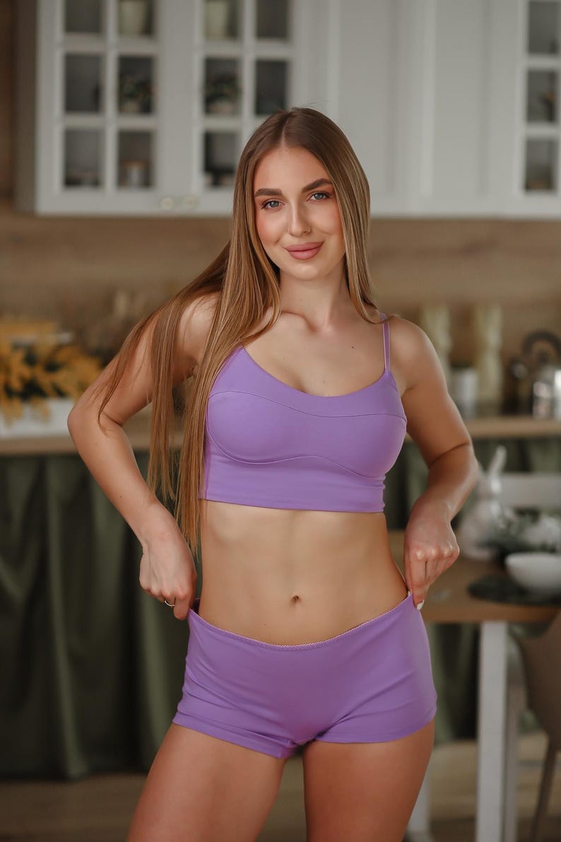 May include: A solid light purple two-piece set consisting of a cropped camisole top with thin shoulder straps and a matching pair of fitted shorts. The fabric appears smooth and matte, featuring clean seams along the bust line and hem.