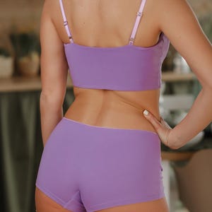 May include: A lavender two-piece set consisting of a cropped camisole top with thin adjustable shoulder straps and matching boy-short style underwear. The set features a solid light purple color with a clean, simple design and smooth fabric.