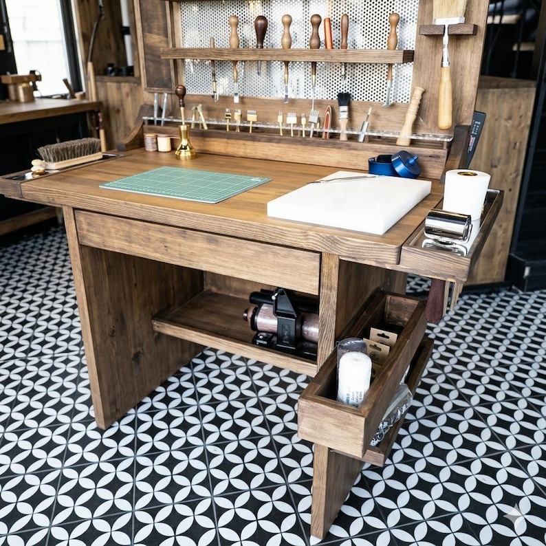 Op de afbeelding: Een houten werkstation voor ambachtslieden in lichtbruin. Het heeft een ingebouwd rek met gereedschap, een groene snijmat en een wit snijplank. Het werkstation heeft een lade en een onderste plank met een machine.