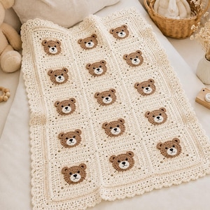 Puede incluir: Manta de bebé de crochet color crema con un patrón repetido de caras de osos de peluche marrones. La manta tiene un borde festoneado y está hecha de hilo suave. Un artículo acogedor y hecho a mano para una guardería.