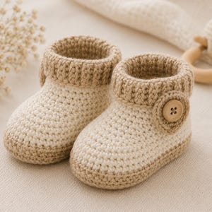 Puede incluir: Un par de botines de bebé de ganchillo hechos a mano en crema y marrón. Los botines tienen un puño acanalado y un cierre de botón. Los colores suaves y neutros y el diseño texturizado crean una estética acogedora y encantadora.
